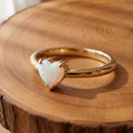 White opal heart gold ring on a tree-trunk slab