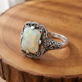 White opal filigree silver ring on a tree-trunk slab