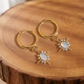 Gold opal star huggie hoop earrings on a tree trunk slab