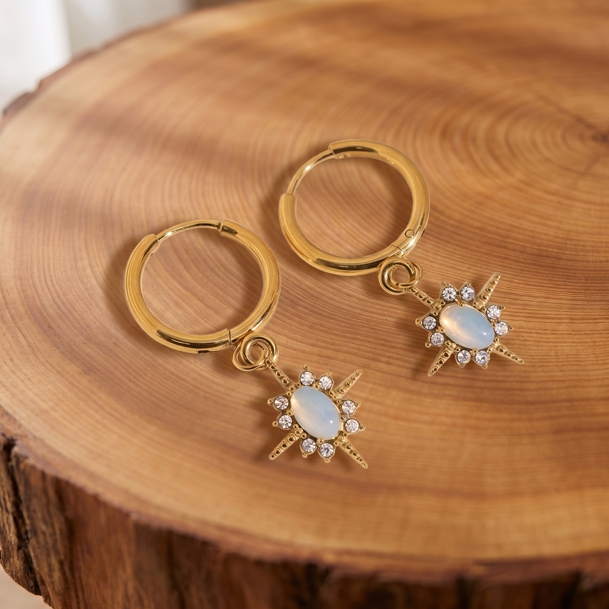 Gold opal star huggie hoop earrings on a tree trunk slab