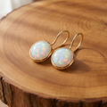 Gold round fire opal drop earrings on a tree trunk slab