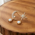 Gold opal moon and star mismatched drop earrings on a tree trunk slab