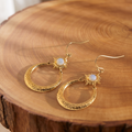 Gold opal sunburst hammered hoop drop earrings on a tree trunk slab